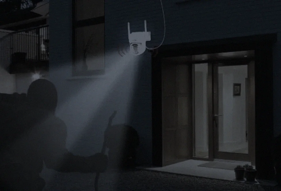 A dark, grey night view of a driveway with a figure near the wall, barely readable